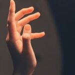 Elegant human hand reaching into soft, warm light creating a serene and artistic effect.